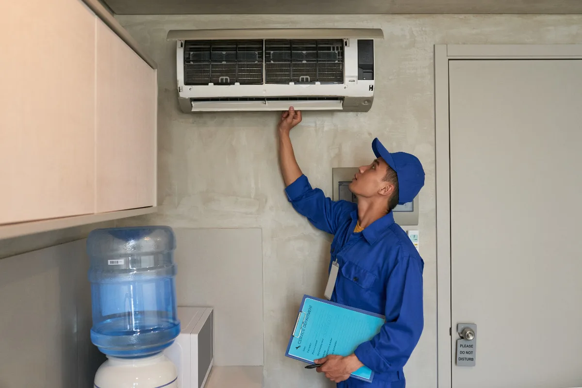 majstor u plavom odelu proverava klima uređaj u zatvorenom prostoru